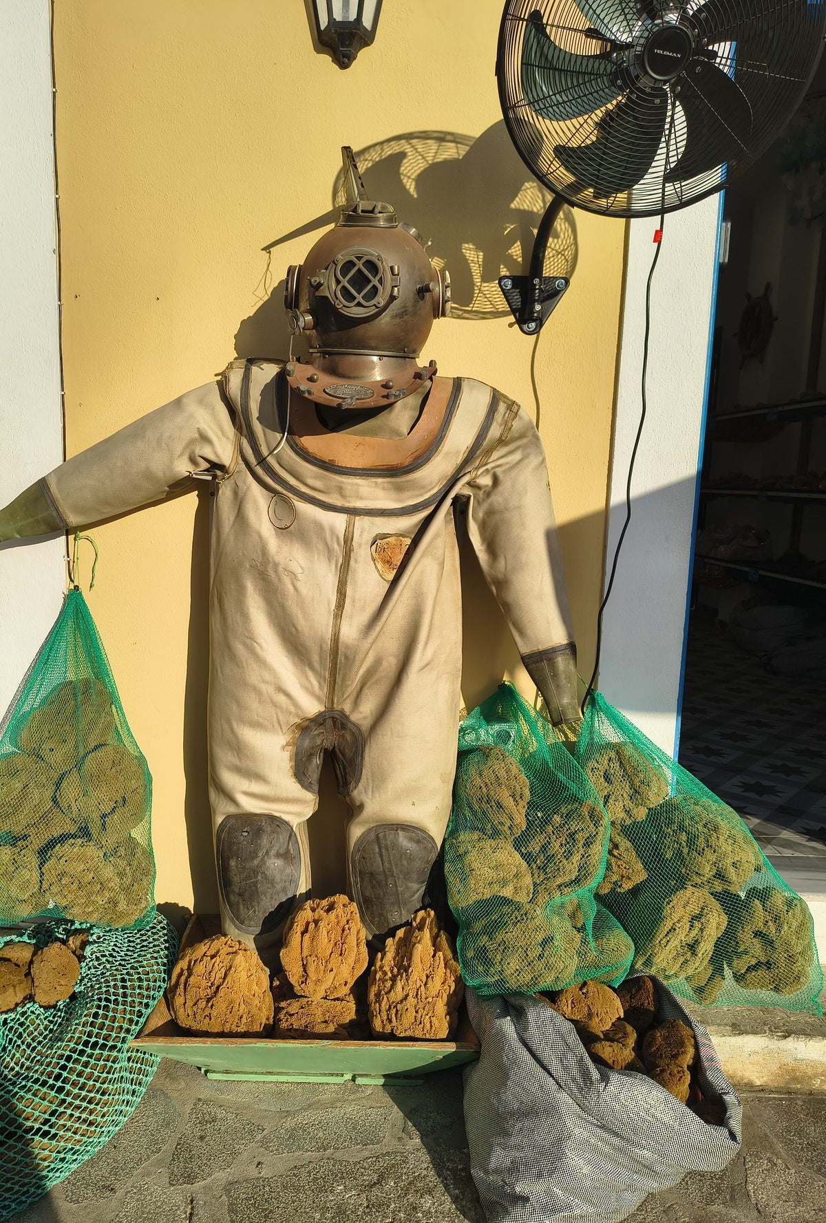 The diving suit and copper helmet standing at the shop door, nets of sponges hanging from its gloves